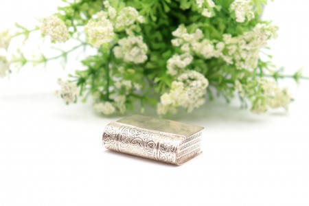 Caixa de comprimidos em prata em forma de livro com gravados na lombada